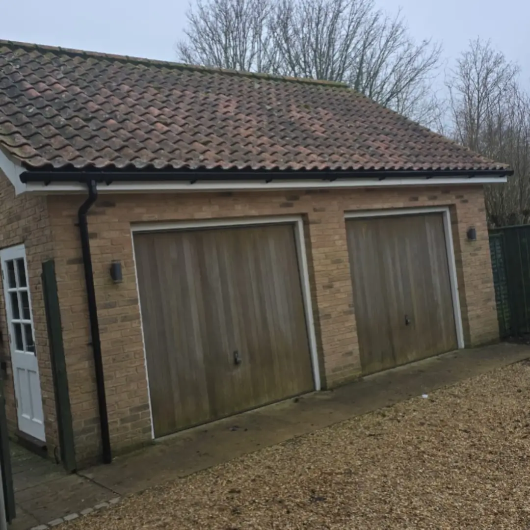 Newly installed maintenance-free black uPVC guttering and white fascia boards on a detached brick double garage by Norfolk Exterior Solutions